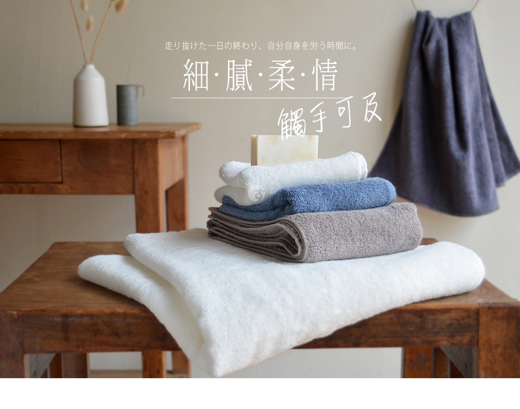 Lisse 蓬鬆柔感有機棉浴巾，疊放著白色、藍色、灰褐色浴巾，另有一條深藍色浴巾懸掛。