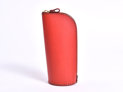 紅色皮革製成的直立式收納筆袋，側邊縫線清晰，頂部配有金色拉鍊和皮革拉環。