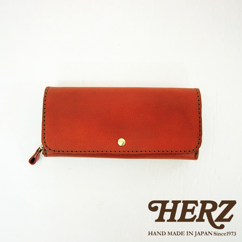 橘紅色皮革長夾，寬口設計，附有側邊拉鍊與金色釦環，邊緣以深色縫線處理，展現職人手作質感。