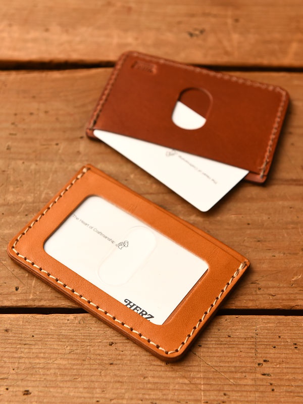 兩件式職人手作皮革橫式票券收納夾，皆為淺棕色皮革，搭配米白色車縫線。其中一件收納夾內嵌透明塑膠隔層，並印有品牌標誌。