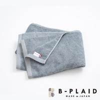 一條灰藍色、觸感柔軟的薄手鱗紋浴巾，帶有灰色的邊緣和一個標有「B-PLAID」及日本國旗圖案的白色標籤。