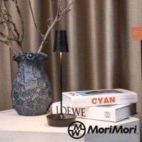 黑色金屬復古氛圍燈，圓形底座，燈罩呈錐形，搭配乾枯樹枝和一個深灰色帶紋理的花瓶，背景為棕色布簾。