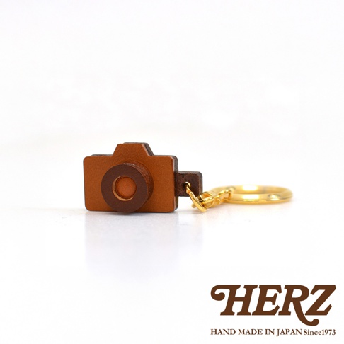皮革製成的手機造型鑰匙圈，主體為棕色，鏡頭部分為深棕色。附有金色金屬鑰匙環。