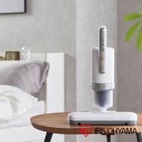 白色與銀色搭配的直立式除塵蟎機，具有銀色提把和透明集塵筒，底部為銀灰色扁平吸頭，放置於木紋圓桌上。