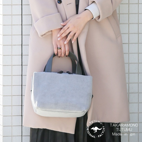 TUTUMU 品牌 Suede tre tote 方形兩用托特包，為灰色絨面材質，搭配黑色皮革提把，由一位身著米色大衣的女性手持。