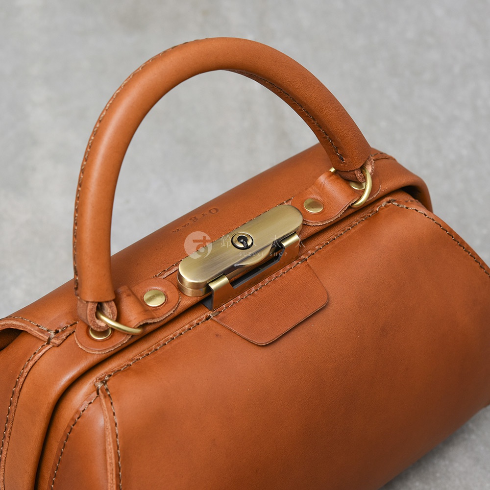 職人手作皮革Organ兩用口金手提包，呈現經典棕色，包身以高品質皮革製成，搭配復古銅色金屬口金鎖扣與提把，整體風格簡約大方。