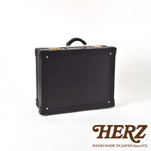 黑色皮革手提行李箱，帶有金色金屬鎖扣、鉚釘和皮革提把，呈現英倫風格。