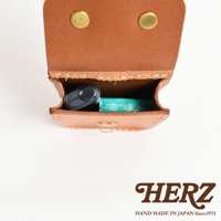 職人手作皮革經典腰袋，採用天然棕色皮革製成，設有兩顆金色金屬釦，袋內可見一黑色電子煙和一盒綠色薄荷糖。