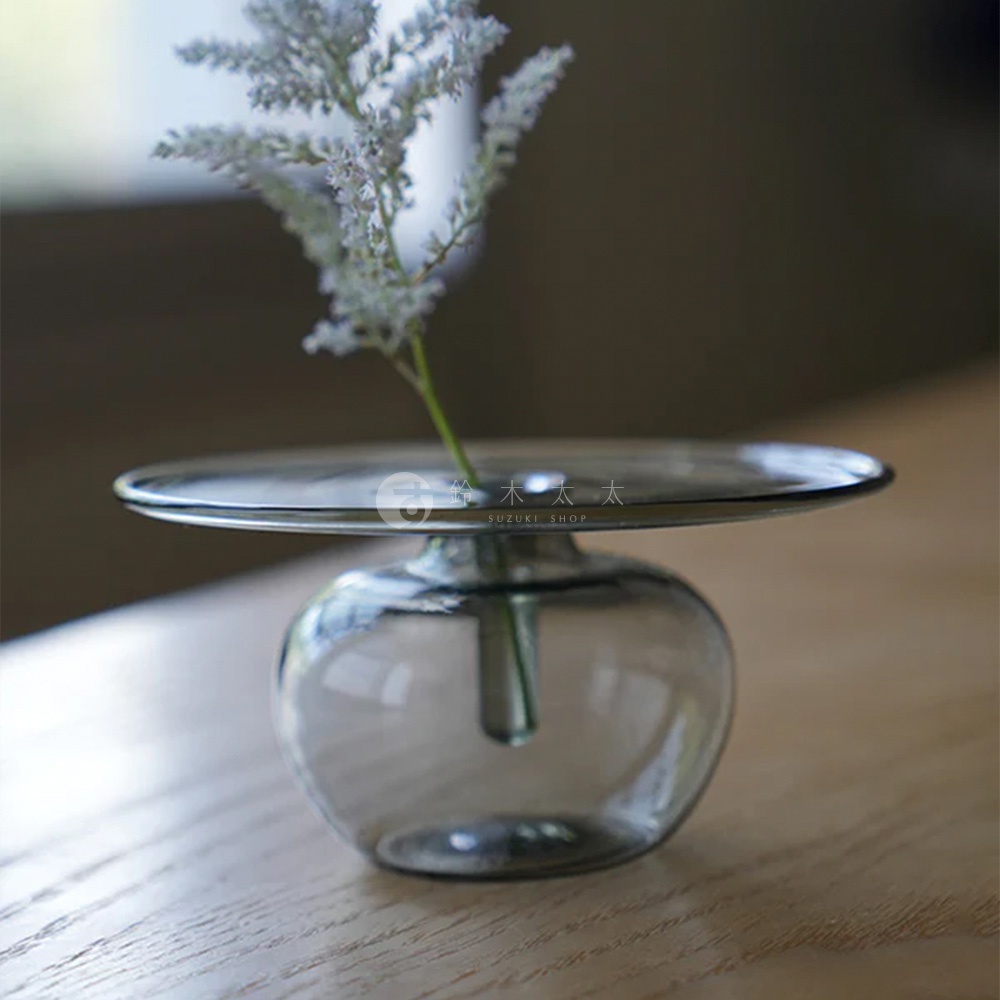 AXCIS Lua 多功能線香玻璃花器，透明玻璃瓶身搭配盤狀上蓋，插著一株淡紫色的小花，擺放在木質桌面。