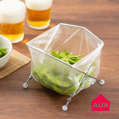 金屬框架垃圾架，內襯透明塑膠袋，裝有綠色毛豆，架子帶有四個帶白色圓形底座的金屬支腳，放置在木桌上。