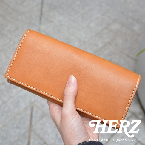 一只手拿著駝色軟皮長夾，夾子邊緣有白色縫線。