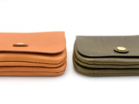 兩款職人手作皮革長夾，一款為棕褐色，另一款為墨綠色，皆採用皮革材質，並配有金色按扣，設計簡潔實用。