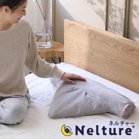 淺灰色瑜珈感安睡枕，外層為棉質布料，呈現人體工學設計，提供頸部與肩部支撐，擺放在白色床鋪上，一旁有女性坐姿。