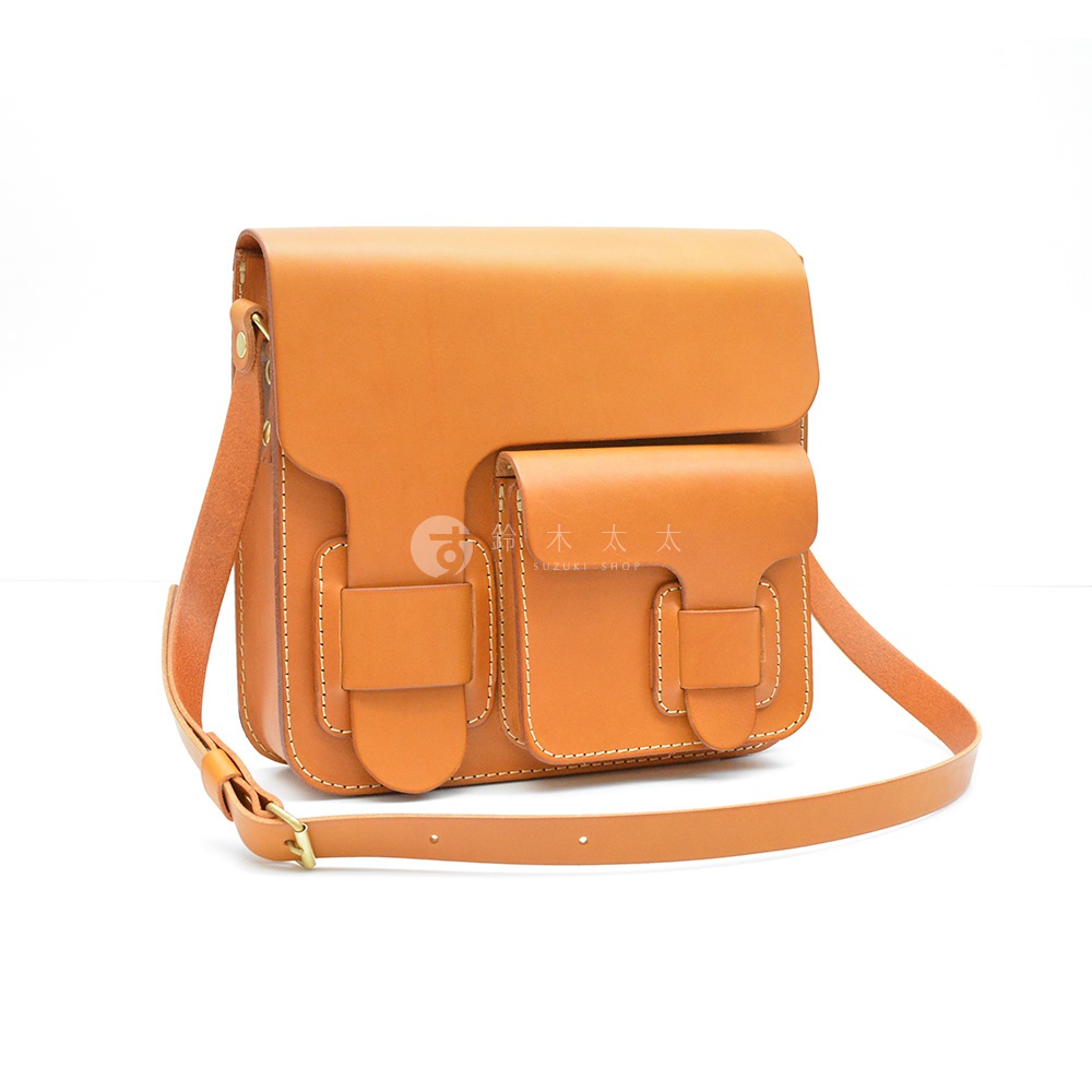 職人手作皮革經典厚實單肩包，採用光滑的淺棕色皮革製成，附有帶有搭扣的翻蓋和兩個前置口袋。包包的邊緣有明顯的白色縫線，並配有可調節的皮革肩帶。