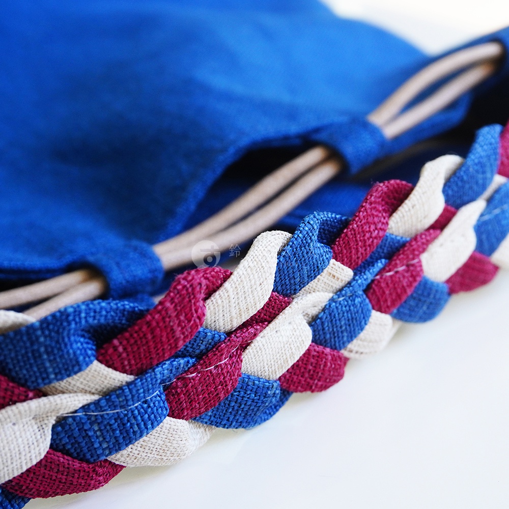 BAN INOUE 麻花辮束口手提包，藍色主體搭配藍、白、紅三色交織的麻花編織提把，材質為天然材質。