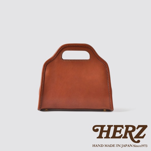 職人手作皮革單肩兩用拱型手袋，呈現自然棕色皮革，擁有經典拱形提把與俐落縫線，底部設有金屬腳釘，可斜揹或手提。