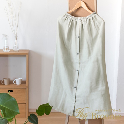 淺綠色棉紗混紡快乾平口鬆緊浴巾浴裙，正面有按鈕設計，懸掛在木質衣架上，背景為白色牆壁與木製層架。