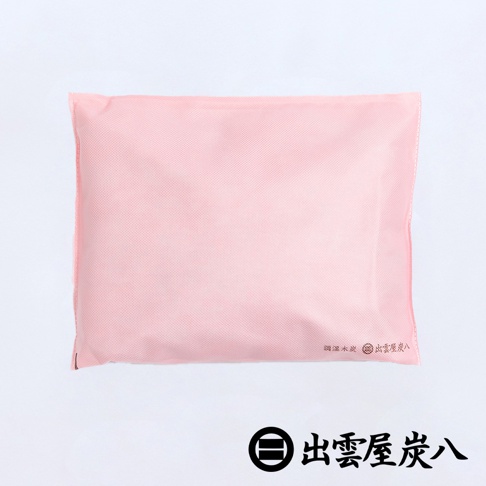 這是一款淡粉色的長方形出雲屋炭八調濕木炭袋，採用雙層不織布材質製成，右下角印有細緻的品牌標誌與文字，整體設計簡約實用，適合車內或室內空間除濕與淨味。