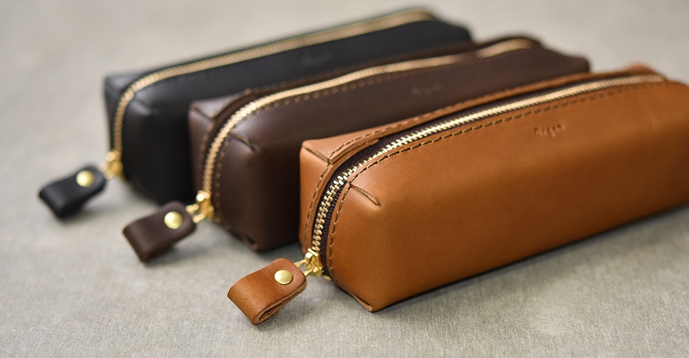 三款職人手作皮革Organ箱型收納筆袋，分別為黑色、深棕色和淺棕色，皆採用光滑皮革材質，搭配金色拉鍊與同色系皮革拉環。