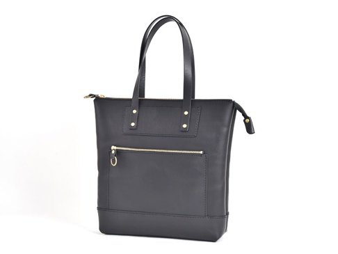 黑色皮革直式拉鍊托特包，附有兩個頂部提把，正面有一個拉鍊口袋和一個貼袋，底部有金色鉚釘裝飾。