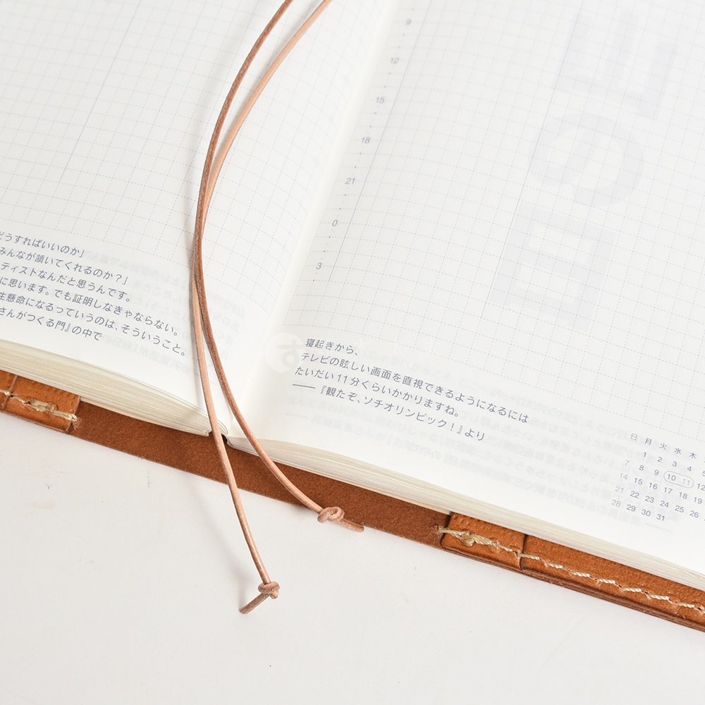 皮革筆記本內頁，有網格線和一些日文文字，還有兩個細長的皮革綁繩。