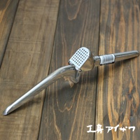 銀色不鏽鋼壓蒜器，帶有圓孔的壓蒜槽和一個長柄，置於深色木紋背景上。