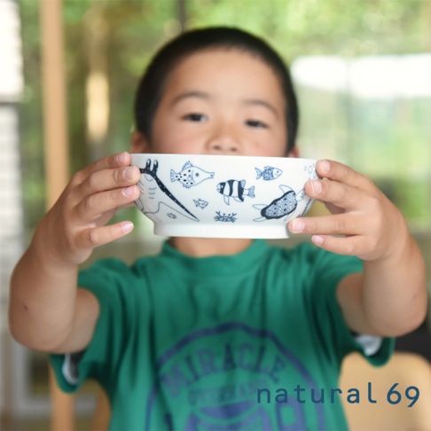 一個小孩手持白色陶瓷碗，碗身繪有藍色線條的海洋生物，包括魚、海龜和螃蟹。