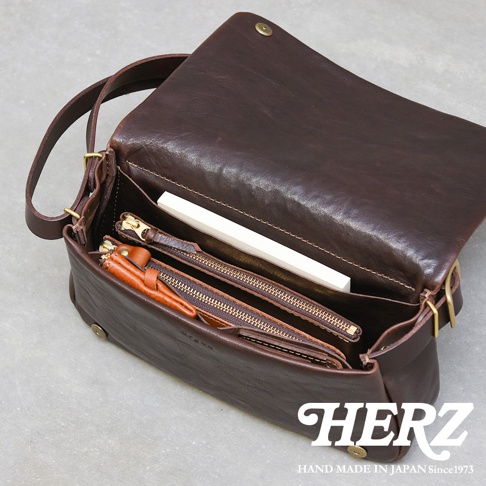 深棕色皮革斜背包，翻蓋設計，內部可見拉鍊夾層、文件和零錢包，材質為Genuine Leather。