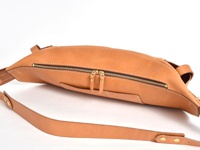 職人手作皮革大容量斜背包，採用天然皮革材質，呈現溫潤的淺棕色調，包身線條流暢，設有雙拉鍊主袋，搭配可調節的皮革背帶，整體簡約實用。