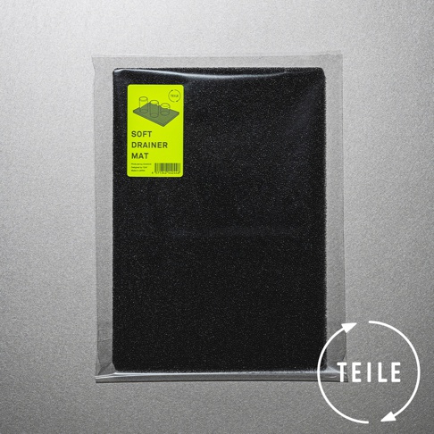 黑色廚房速乾瀝水墊，材質為細緻的發泡材質，表面有細小顆粒。左上角貼有黃色標籤，印有品牌標誌、產品名稱「SOFT DRAINER MAT」及示意圖。產品整體以透明塑膠袋包裝。
