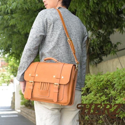 男性背著一個棕褐色皮革製的三用學生包，包身有兩個皮帶扣和一個提把，整體呈現傳統歐式風格。