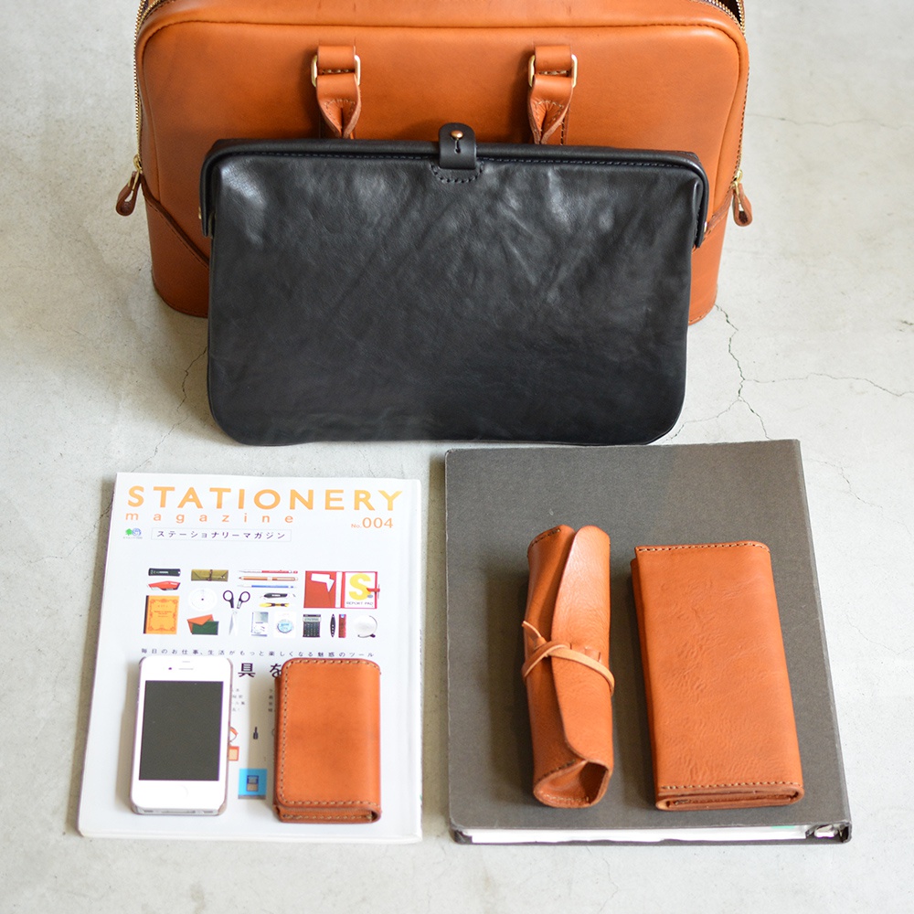 職人手作皮革Organ商務公事包 G-40，展示了棕色皮革公事包、黑色皮革長夾、棕色皮革手機、棕色皮革卡夾、捲筒式筆袋及筆記本，擺放於灰色大理石紋背景上。