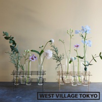 兩個金屬支架，分別裝有玻璃花器。左側為黑色金屬支架，內有六個玻璃管，插著綠葉、紫色小花、白色圓形花和綠色枝條。右側為金色金屬支架，內有六個玻璃管，插著淡紫色花、藍色花、白色小花和綠葉。