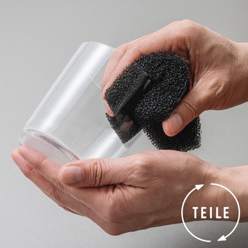 一雙手正握著黑色網狀超細纖維清潔海綿，擦拭著透明玻璃杯。