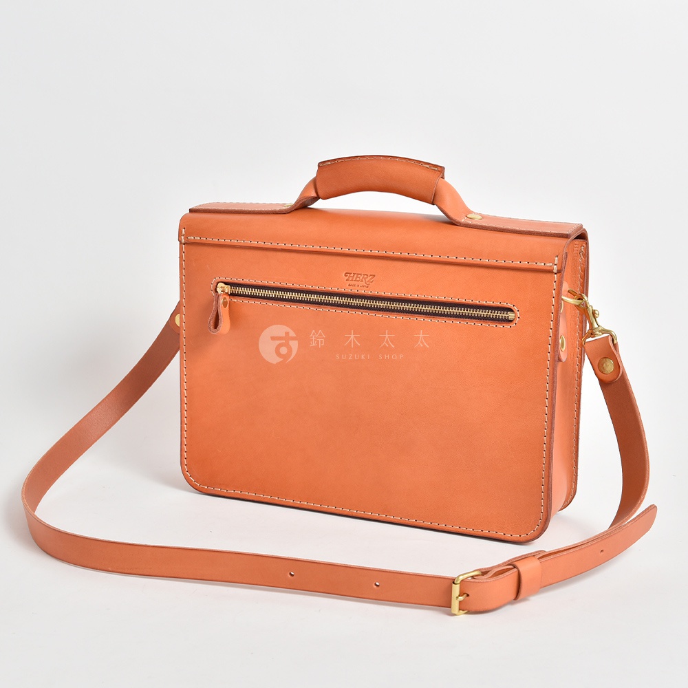 橘色皮革製成的手提公事包，配有頂部提把、可拆卸肩帶、拉鍊前袋及三扣設計。
