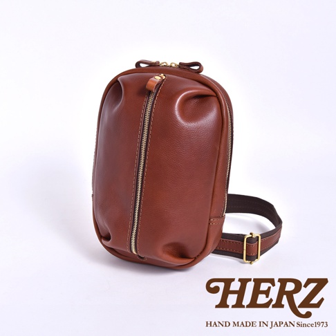 日本HERZ職人手作Stare皮革立體運動斜背包，深棕色，正面有拉鍊，背帶有金屬扣環，下方有HERZ品牌Logo。