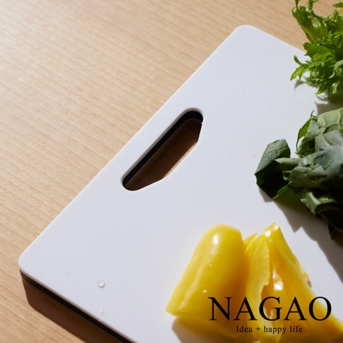 SHINKA 雙面抗菌耐熱砧板，白色，帶有長方形鏤空提手。砧板上擺放著切塊的黃色甜椒，上方有綠葉蔬菜。