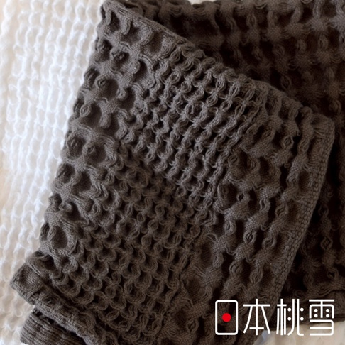 一件深棕色、帶有蜂窩織紋的今治鬆餅浴巾，質地柔軟，部分堆疊在白色背景上。