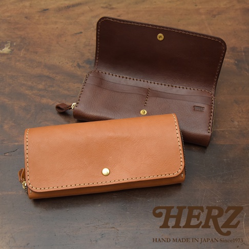 兩款職人手作皮革長夾，一款為閉合狀態的棕褐色長夾，另一款為展開的深棕色長夾，皆為寬口設計，配有金屬按扣與拉鍊，縫線清晰可見。