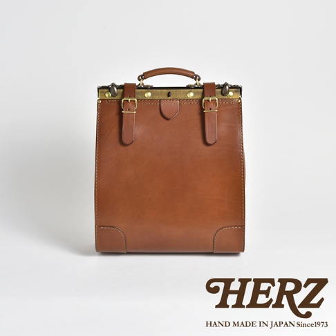 職人手作復古皮革後背包，採用棕色皮革，搭配黃銅色金屬口金、扣環與鉚釘，上方有提把，兩側有可調節的皮帶，設計簡約耐用。