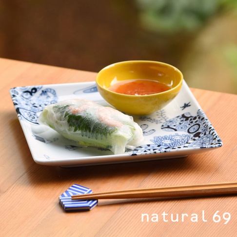 一個方形白色餐盤，飾有藍色花紋，上面放著一個越南春捲和一小碗黃色沾醬。