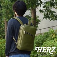 職人手作綠色皮革長方型多口袋後背包，展示於戶外。背包採用光滑皮革材質，設有拉鍊開合和外部拉鍊口袋。