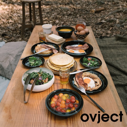 木質餐桌上擺放著豐盛的早餐，包含煎餅、培根、荷包蛋、沙拉和湯，以及裝有小番茄的黑色琺瑯碗。