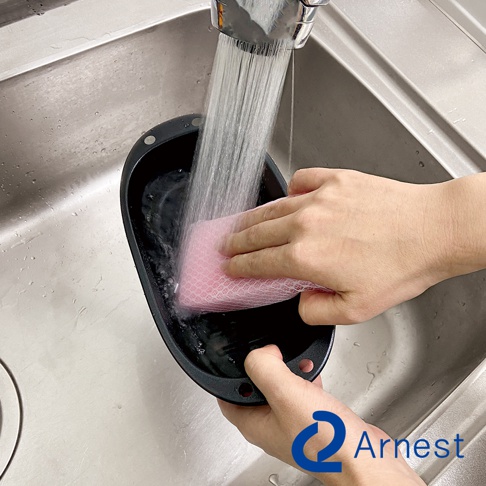 Arnest 多功能微波料理器正在水槽中被沖洗，用海綿清潔。