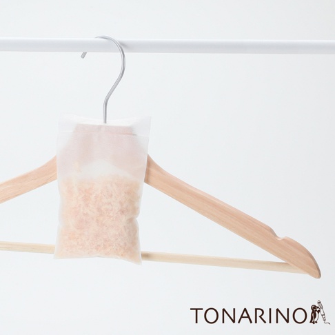 一個透明的防潮消臭檜木除濕包，內含淡黃色細小檜木顆粒，懸掛在一個淺木色衣架上，衣架掛在白色掛架上。