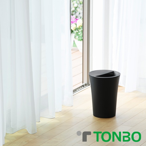 黑色圓形半開垃圾桶，容量7.3L，置於木質地板上，背景為白色紗簾與落地窗外的綠意。