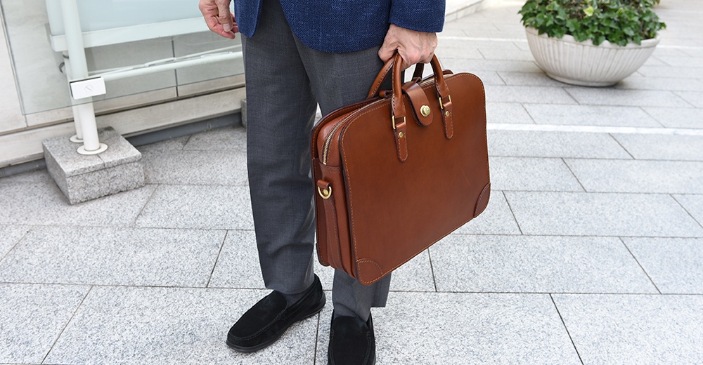 棕色皮革三層收納兩用商務公事包，配有金色拉鍊、鎖扣和可拆卸肩帶。