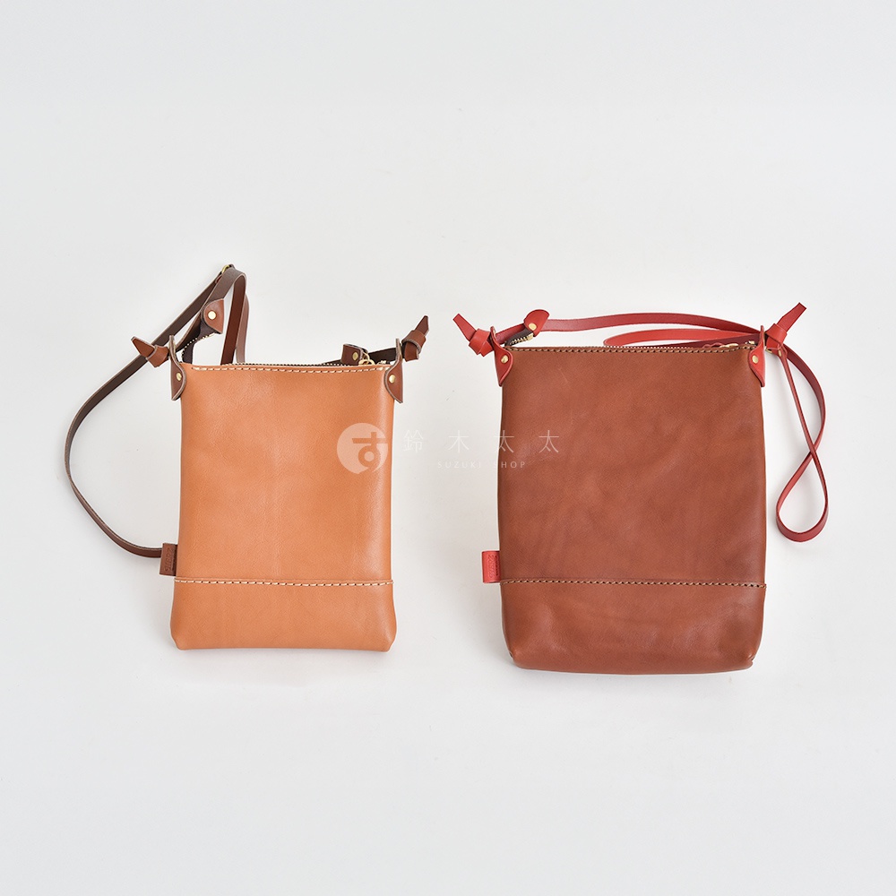 兩款皮革直式隨身單肩包，一款為淺棕色，另一款為深棕色，皆配有可調節的斜背帶，簡約設計，質感皮革。