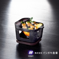 黑色鑄鐵烤盤鍋爐組，烤盤上擺放著多塊煎烤過的扇貝，旁邊配有檸檬片和綠葉裝飾。鍋爐下方有燃燒的火焰，整體置於深色木紋桌面上。