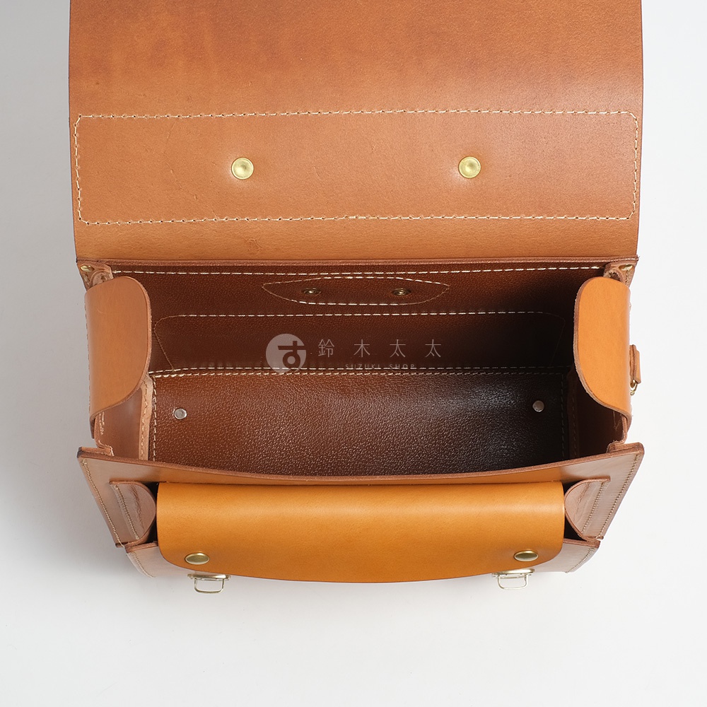 打開的棕色皮革橫式書包內部，上方有金色金屬釦，內襯為深棕色皮革。